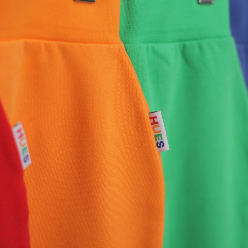 red, orange, green and blue joggers on a hanger by Hues Clothing
