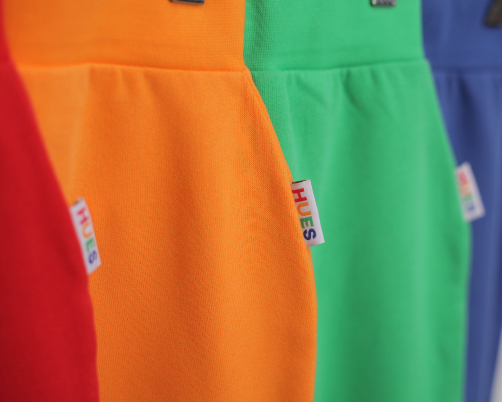 red, orange, green and blue joggers on a hanger by Hues Clothing